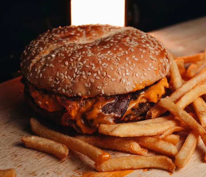 Hamburguesa con queso y papas fritas sobre una tabla de madera.