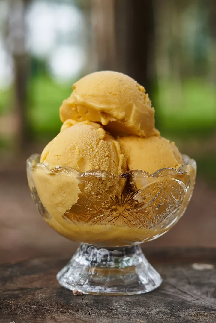 Tres bolas de helado amarillo en una copa de vidrio.