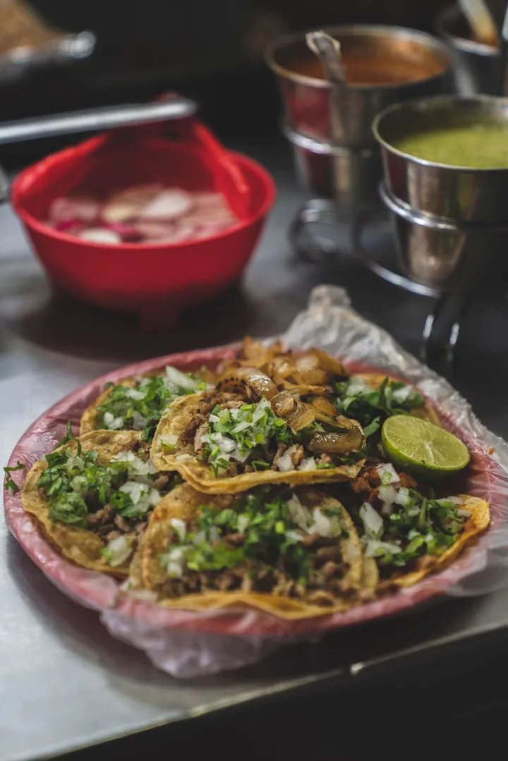 Tacos con cebolla, cilantro y limón servidos en un plato junto a las salsas.
